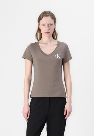Smeđi pamučni T-shirt s V-izrezom, kratkim rukavima i malim bijelim CK logotipom na lijevoj strani grudi. Glatka tekstura, ležeran kroj.