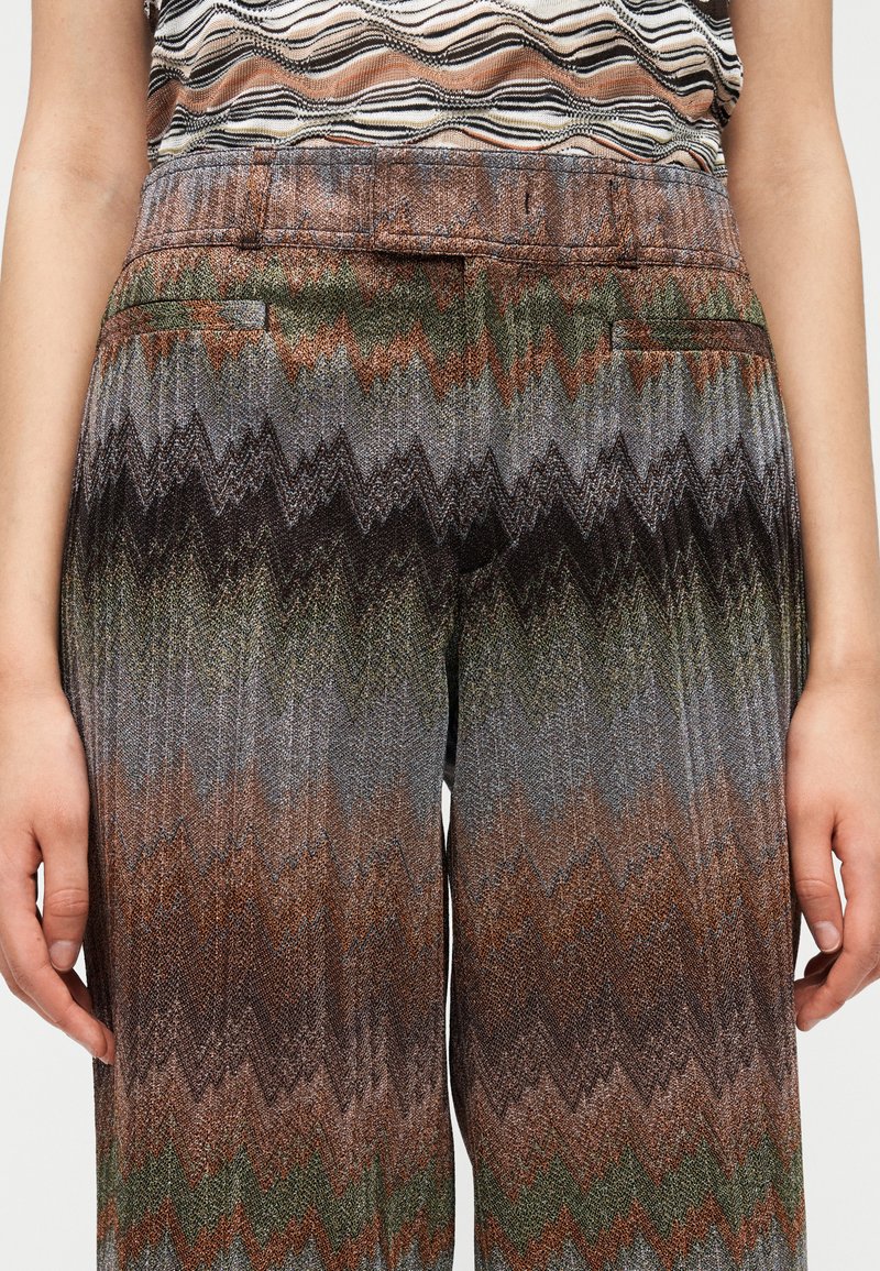 Multicolored, patterned high-waisted trousers with a zigzag design in earth tones of brown, green, and gray. Features side pockets.