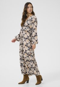 Maxikleid aus bedrucktem Stoff mit schwarzen, beigen und goldenen Palmenblättern; lange Ärmel, V-Ausschnitt und geschichteter Rockdetails.