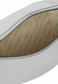 Borsetta bianca in pelle con zip aperta che mostra l'interno beige foderato con il motivo del testo "HARBOUR 2ND" e loghi a forma di ancora.