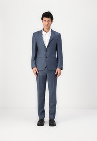 Dunkelblauer Anzug mit schlanker Passform, einreihiger Jacke, geraden Hosen und einem weißen Hemd mit Knöpfen. Schwarze Schuhe runden den Look ab.