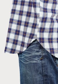 Short-sleeved, blue and white plaid shirt with orange accents, featuring a textured fabric and rounded hem, worn over blue denim jeans.