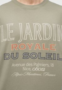 Μπλουζάκι με κείμενο "Le Jardin Royale du Soleil" και διεύθυνση "Avenue des Palmiers, 18 Nice, 06012 Alpes-Maritimes, Γαλλία" σε διάφορες γραμματοσειρές.