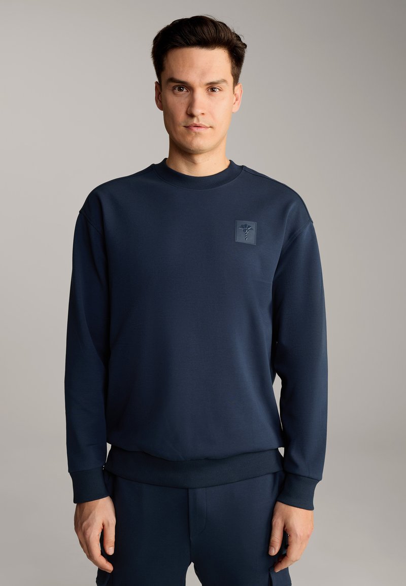 Felpa blu navy con scollo a girocollo, polsini e orlo a coste, caratterizzata da un piccolo logo in rilievo sul petto. Tessuto morbido e texturizzato.