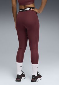 Bordeaux leggings med en sort PUMA-logo på taljen. Stoffet er glat, og designet inkluderer en tætsiddende ankel-længde stil.