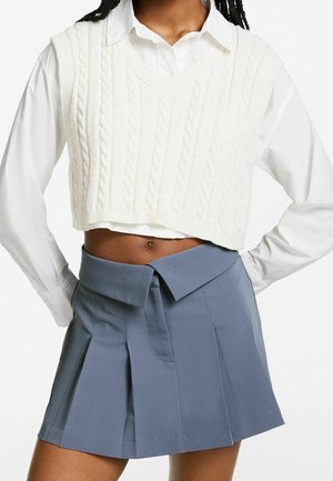 Biały kamizelka z warkoczykiem, przerywana na krótko, noszona na białej koszuli z kołnierzykiem, w połączeniu z szarym plisowanym mini spódnicą z szerokim pasem i detalem w postaci węzła.