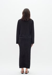 Black knit sweater with long sleeves paired with a fuzzy black maxi skirt. Textured fabric, slim-fit silhouette, and ankle-strap black sandals.