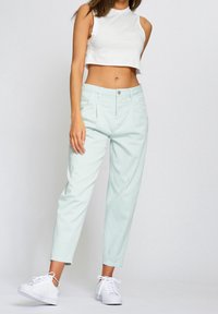 Světlé mátově zelené kalhoty s vysokým pasem a volným střihem, s vroubkovanými záhyby a předními kapsami, doplněné bílým krátkým tílkem a bílými teniskami.
