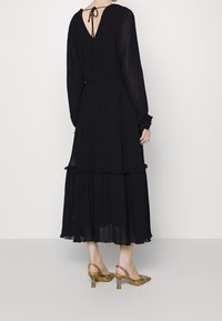 Abito maxi nero plissettato con maniche lunghe, scollo a V sul retro e dettagli a volant all'orlo. Abbinato a tacchi a punta con motivo.