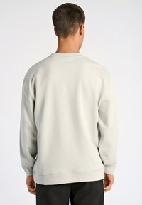 Sudadera gris claro con mangas largas, cuello redondo y puños acanalados. Tejido suave, corte relajado y diseño minimalista sin logotipos visibles.