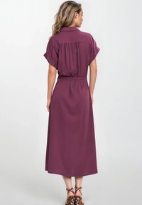 Dopasowana, midi sukienka w głębokim śliwkowym kolorze, z krótkimi, zwiniętymi rękawami, plisowanym tyłem i wiązanym w pasie dla podkreślenia sylwetki. Połączona z sandałami na obcasie w zebrę.