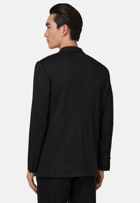 Svart kavaj med en strukturerad design, skräddarsydd passform och slät textur. Har en slagkrage och knäppte manschetter.