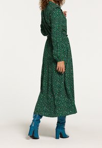 Grön blommig omslagsklänning med långa ärmar och krage, åtverksad midja. Matchad med blå texturerade knähöga stövlar.