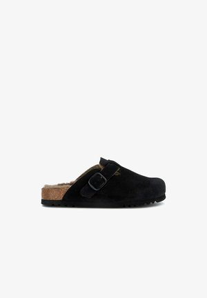 Black suede clog with a cork midsole, fuzzy lining, adjustable buckle strap, and textured rubber sole, designed for slip-on ease.