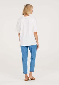 Weißes Baumwoll-T-Shirt mit lässigem Schnitt, kurzen Ärmeln und Rundhalsausschnitt, kombiniert mit hellblauen Jeans und braunen Sandalen.