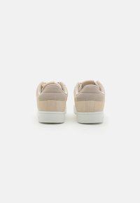 Beige semskinn sko med en jevn tekstur, myk polstret krage og hvit gummiksole. Bakfra vises rund hæl og ren design.