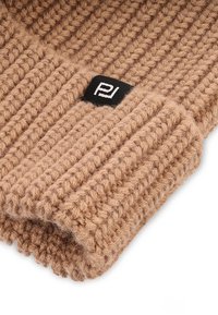 Beżowa czapka dzianinowa z prążkowaną fakturą i zagiętym mankietem. Posiada małą czarną metkę z białym logo z boku.