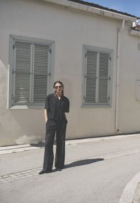 Ensemble noir transparent composé d'un haut court ample et d'un pantalon large, présentant des motifs floraux complexes. Des lunettes de soleil complètent le look.