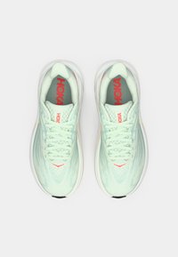 Ανοιχτό πράσινα αθλητικά παπούτσια HOKA με άσπρες σόλες και κόκκινο λογότυπο, φωτογραφημένα από ψηλά σε λευκό φόντο.