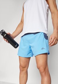 Light blue athletic shorts with a black waistband and pockets. A white sleeveless top, and a black water bottle with silver accents.