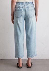 Light blue, wide-leg jeans with an elasticated waistband. Features two back pockets and raw hem detailing at the cuffs.