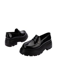 Mocasines de charol negro con suela de goma gruesa y una tira decorativa en el empeine. Superficie lisa con un acabado brillante.