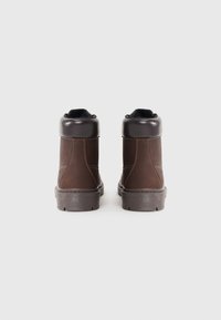 Botas de tobillo de cuero marrón con suela de goma gris, que cuentan con un cuello acolchado y un sutil detalle de costura en los laterales.