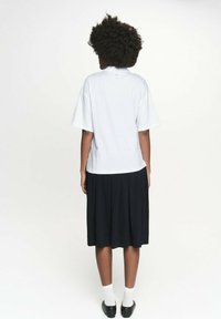 Biała koszulka z krótkim rękawem, luźny krój, w połączeniu z czarną plisowaną spódnicą. Modelka nosi czarne buty i białe skarpetki. Proste tło.