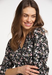 Bluză neagră cu flori, cu decolteu în V, dintr-un material moale, cu mâneci lungi tip balon și un model delicat de flori roz și albe, cu accente verzi.