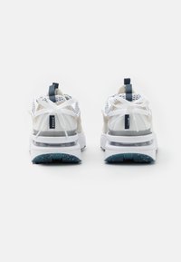 Ett par vita och beigea atletiska sneakers med tjocka sulor och vita snören, visade bakifrån på en helt vit bakgrund.