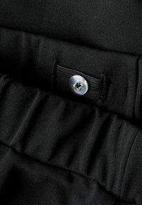 Tissu noir au toucher lisse, doté d'une fermeture à boutons sur le devant et de détails en bande élastique le long de la taille.