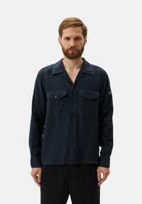 Camisa abotonada de color azul oscuro, hecha de una tela suave, con cuello, dos bolsillos frontales y mangas largas. Diseño minimalista con detalles sutiles.