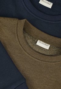Suéteres de cuello redondo en azul marino y verde oliva doblados, con cuellos acanalados y etiquetas de la marca Minymo visibles.