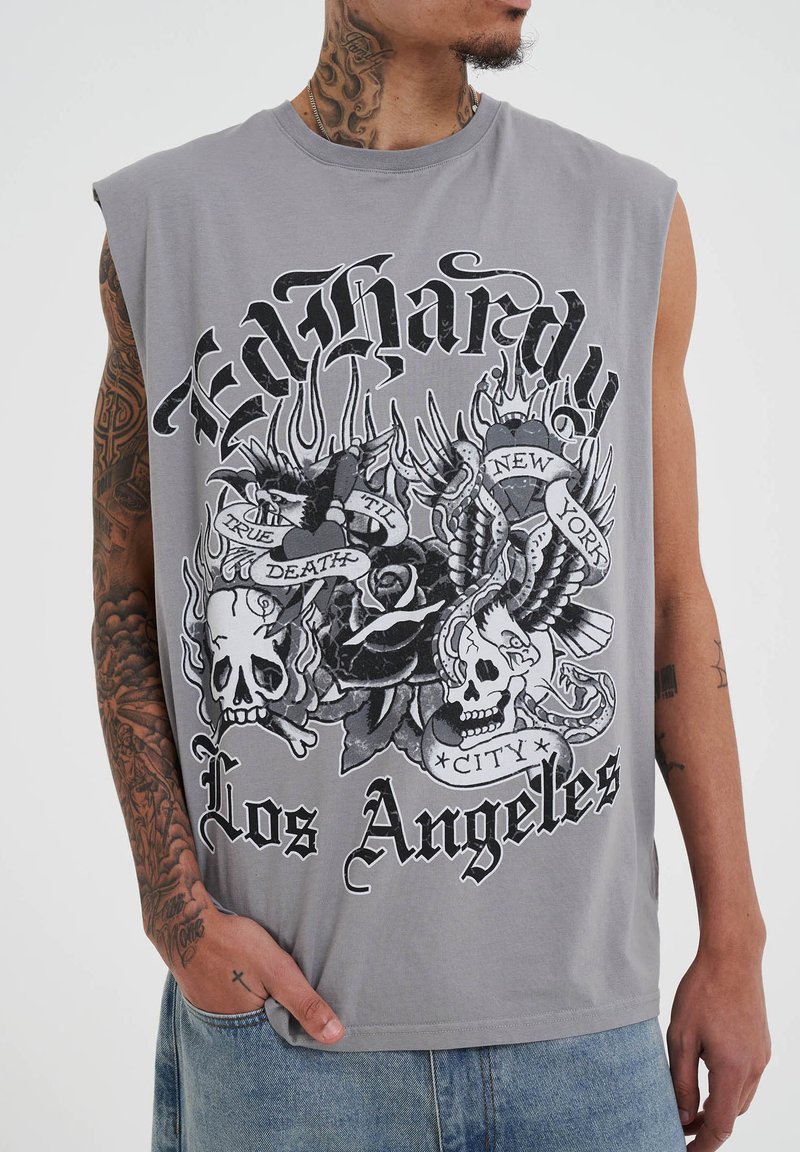 Camiseta sin mangas gris con un diseño gráfico que incluye calaveras, rosas y el texto "Ed Hardy", "Los Ángeles" y "Nueva York". Material de algodón suave.
