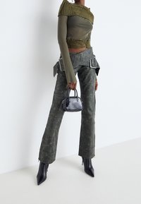 Olivgrön långärmad topp med texturerade detaljer, högmidjade grågröna byxor och en liten svart väska med krokodilstruktur. Spetsiga klackar.