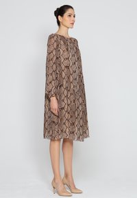 Sukienka w brązowy wzór wężowej skóry z długimi rękawami i luźnym krojem, zestawiona z cielistymi szpilkami. Gładka tekstura i długość do kolan.