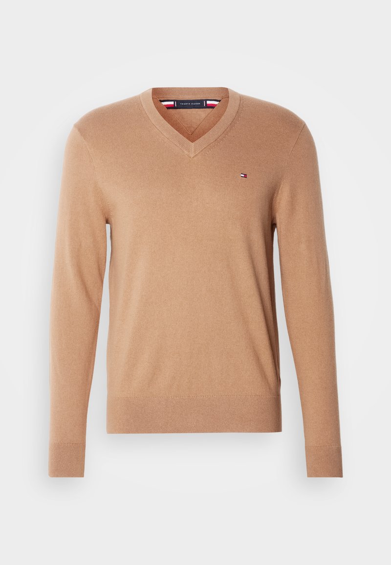 Maglione beige a scollo a V realizzato in morbido tessuto a maglia. Presenta maniche lunghe e un piccolo logo ricamato sul lato sinistro del petto. Texture liscia.
