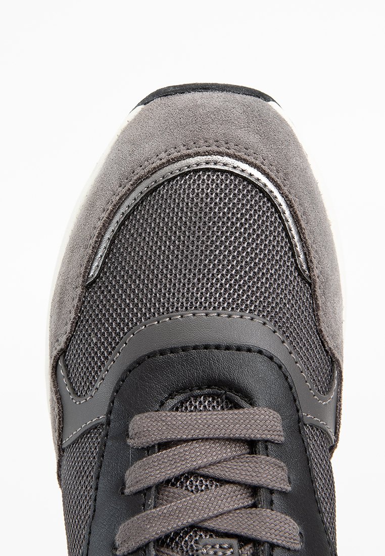 Sneaker grigio scuro realizzato con una combinazione di materiali in suede e mesh, dalla forma arrotondata e con lacci piatti, caratterizzato da un accento metallico lucido lungo il bordo superiore.