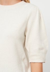 Light beige knit sweater featuring short puffed sleeves, a round neckline, and a soft texture with ribbed cuffs for a snug fit.