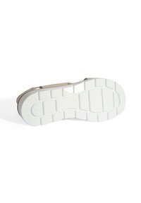 Sneaker met een robuuste witte rubberen zool met een gridpatroon, aangevuld met een lichtbruine bovenkant van stof en een minimalistisch ontwerp.