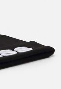 Un bonnet noir en tricot avec un ourlet replié, arborant cinq patchs circulaires brodés en argent à l'avant. Texture douce, design décontracté.