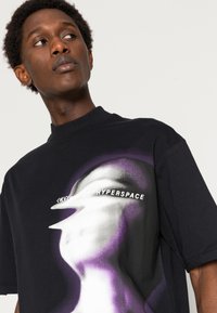 Black oversized T-shirt featuring a purple and white graphic design with the word "HYPERSPACE" across the front. Short sleeves and crew neck.
