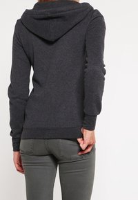 Tmavě šedá bavlněná mikina s kapucí na stahovací šňůrku a žebrovanými manžetami, s hladkým povrchem a přiléhavým střihem.