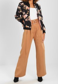 Czarna bomberka w kwiaty z różową podszewką, zestawiona z beżowymi spodniami o szerokich nogawkach z paskiem. Modelka ma na sobie czarne botki za kostkę.