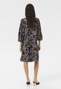 Robe à manches courtes beige avec un motif abstrait bleu foncé, présentant une coupe décontractée et un tissu texturé, atteignant le milieu de la cuisse en longueur.