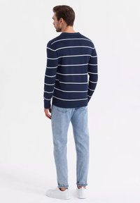 Námořnický modrý pruhovaný svetr s bílými vodorovnými pruhy, kulatým výstřihem a žebrovanými manžetami, v kombinaci se světle modrými džínami a bílými teniskami.