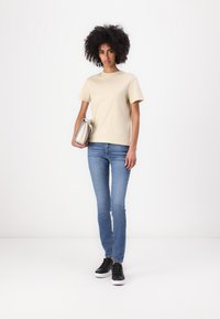 Beige cotton t-shirt, crew neck, short sleeves, paired with light blue fitted jeans and black sneakers. Holding a silver clutch.