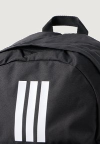 Black fabric backpack featuring a top handle and a zip closure, adorned with three vertical white stripes on the front.