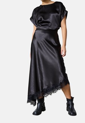 Kvinde iført en sort satin top og asymmetrisk nederdel med blonderkant, kombineret med sorte ankelstøvler med spænder.