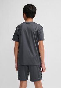 Grau feuchtigkeitsableitendes Sportshirt mit kurzen Ärmeln und passenden Shorts, die an den Seiten schwarze Chevron-Akzente aufweisen.